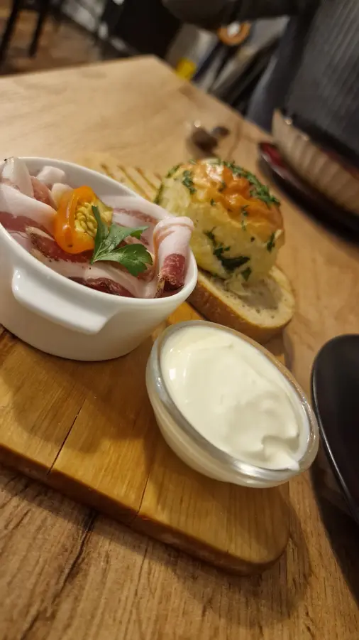 Vorspeise mit Speck, Pfefferoni, Pampuschka und Sauerrahm auf einem Holzbrett
